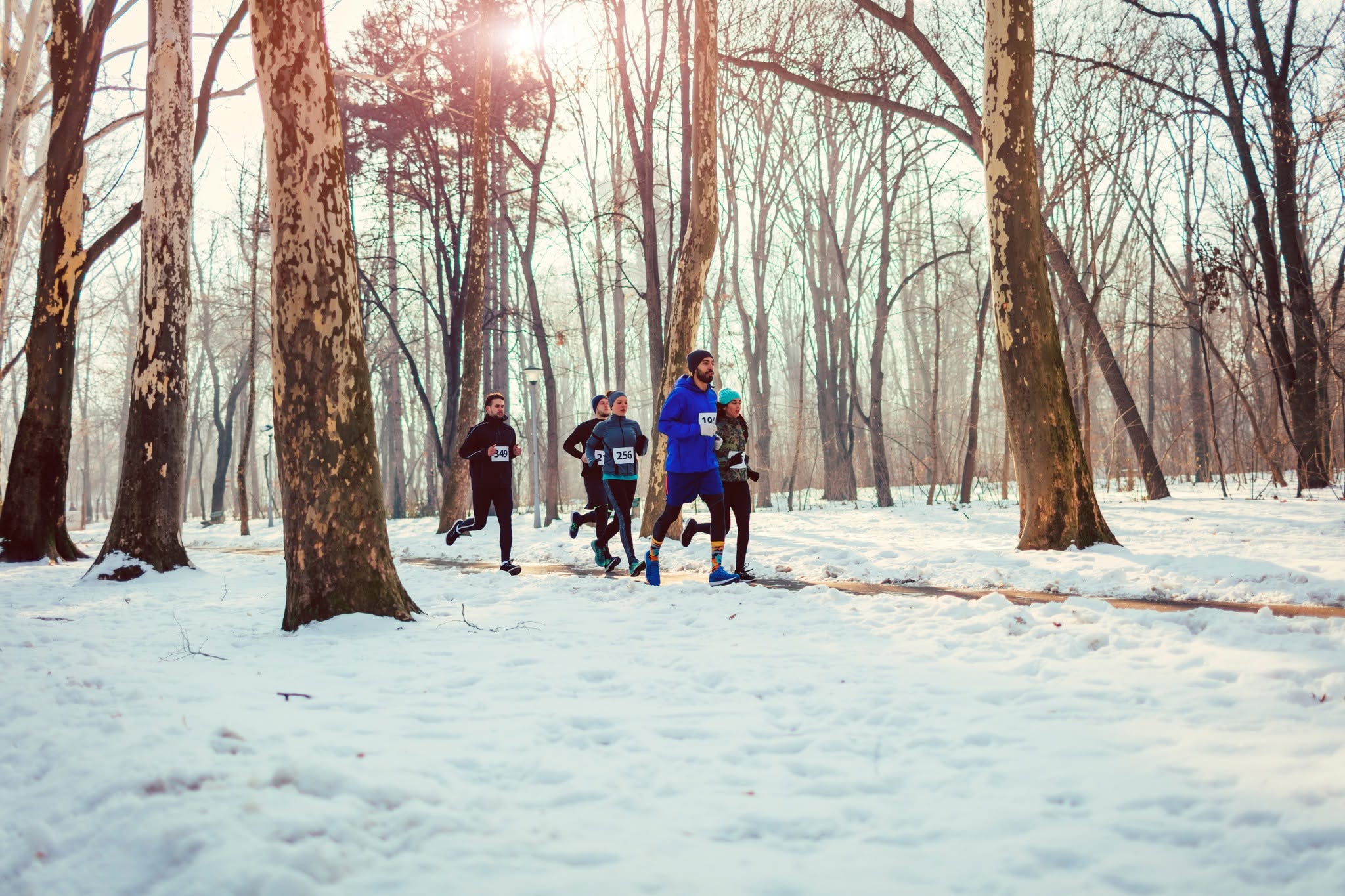 A small group of people run through a forest in winter.